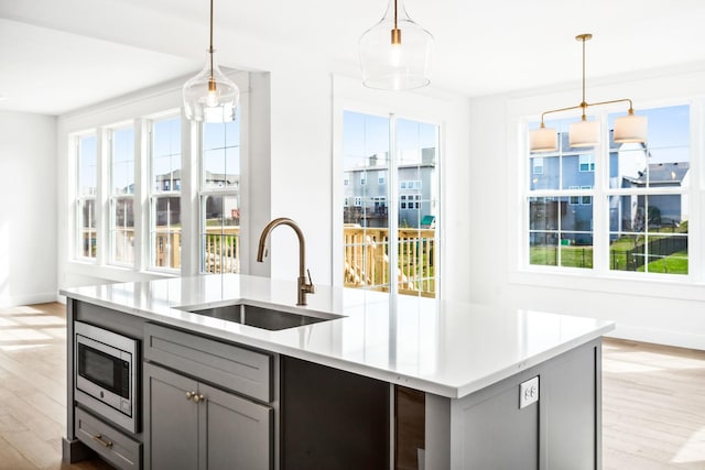 kitchen featuring light wood-style flooring, stainless steel microwave, a sink, light countertops, and gray cabinetry