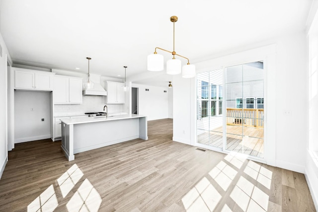 kitchen with custom range hood, light countertops, white cabinetry, backsplash, and light wood-style flooring