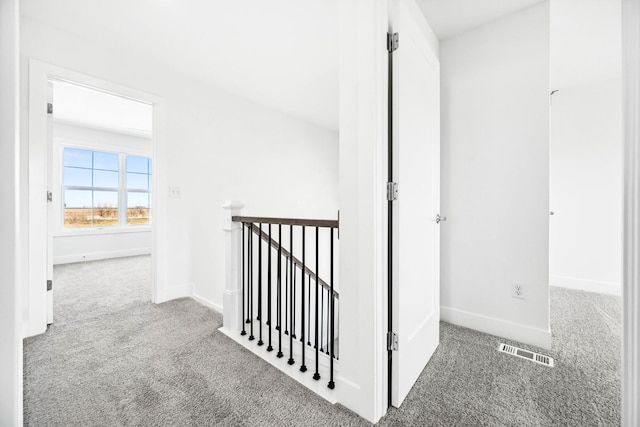hallway with carpet floors, baseboards, an upstairs landing, and visible vents