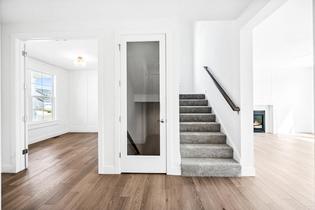 stairway featuring a glass covered fireplace, baseboards, and wood finished floors