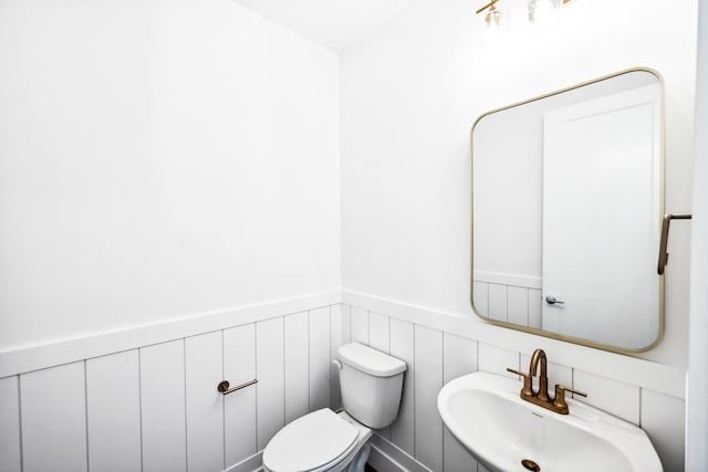half bath featuring toilet, a sink, and wainscoting