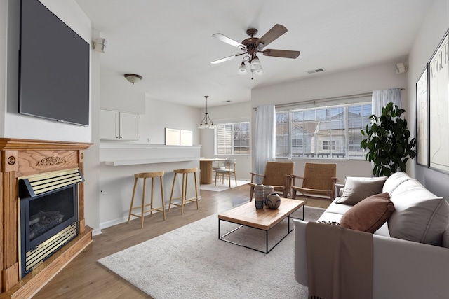 living room featuring light wood-style floors, ceiling fan, a fireplace, visible vents, and baseboards