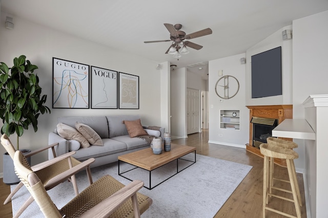 living area with wood finished floors, ceiling fan, and a fireplace with raised hearth