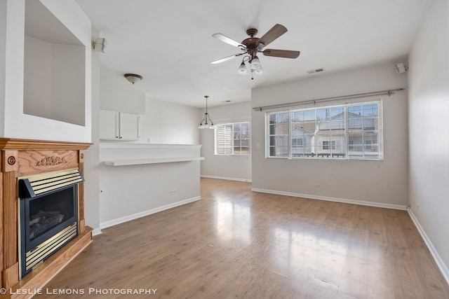 unfurnished living room with baseboards, a ceiling fan, light wood-style floors, and a fireplace