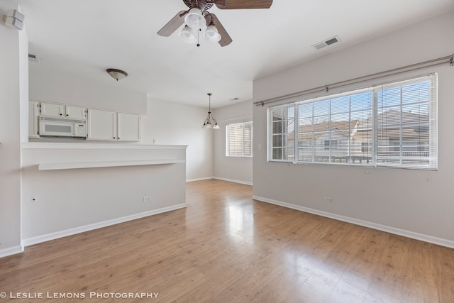 spare room with light wood-type flooring, baseboards, a ceiling fan, and visible vents