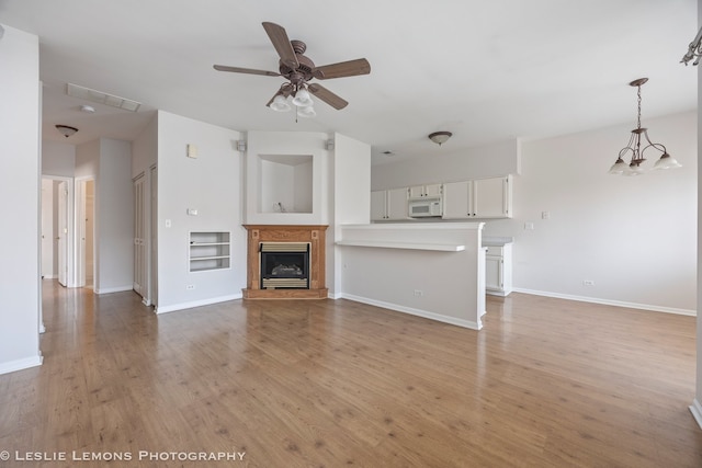 unfurnished living room featuring a glass covered fireplace, light wood finished floors, baseboards, and a ceiling fan