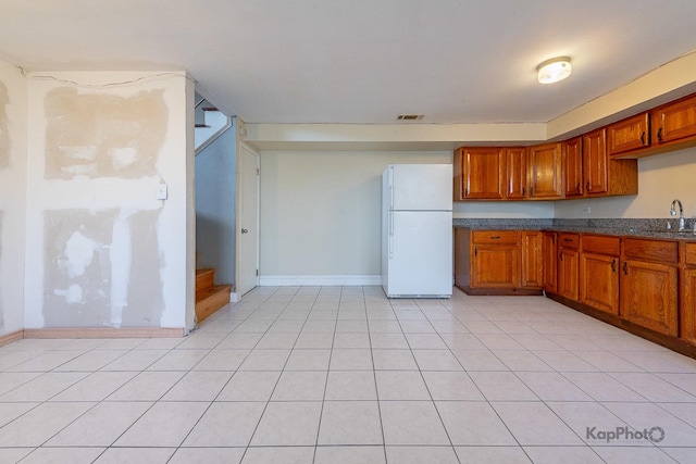 kitchen with a sink, visible vents, brown cabinetry, and freestanding refrigerator