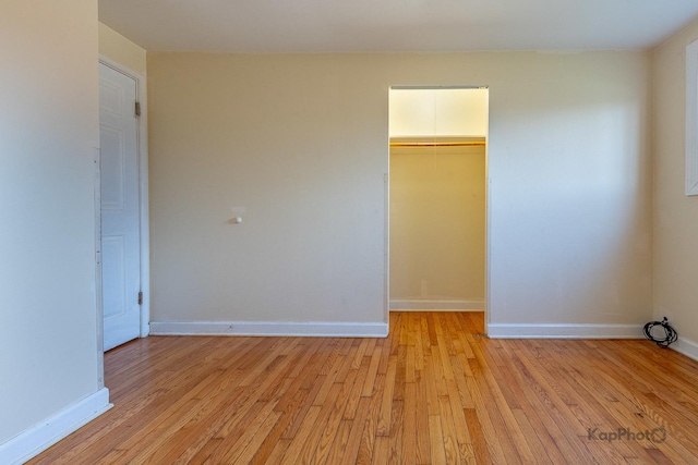 unfurnished bedroom featuring light wood-type flooring, a closet, baseboards, and a walk in closet