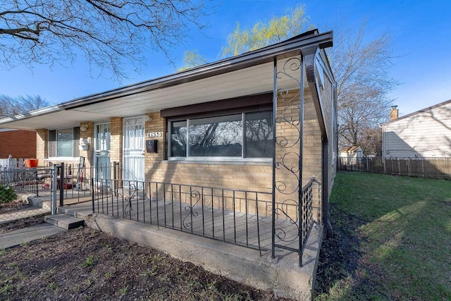 view of front facade featuring a fenced front yard, covered porch, a front lawn, and brick siding