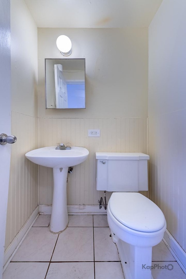 bathroom featuring toilet, tile patterned flooring, a sink, and a wainscoted wall