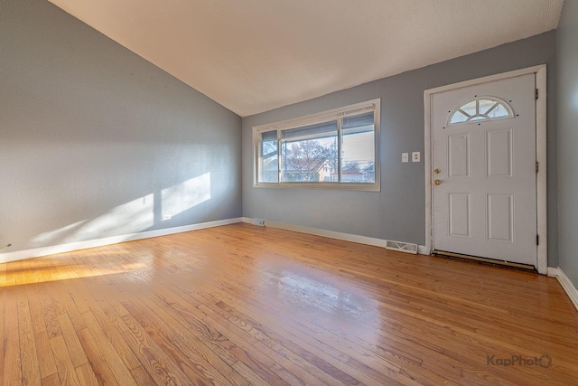 foyer entrance with baseboards, wood-type flooring, lofted ceiling, and visible vents