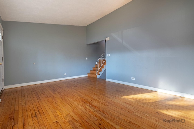 unfurnished room featuring baseboards, hardwood / wood-style flooring, and stairs