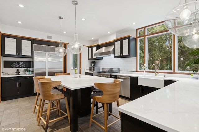 kitchen with tasteful backsplash, wall chimney range hood, a sink, stainless steel appliances, and dark cabinetry