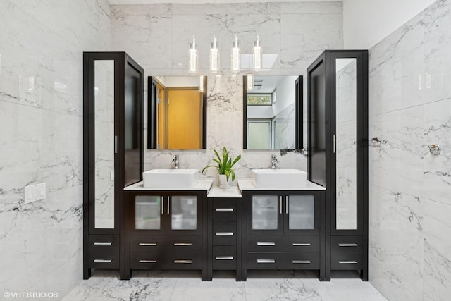 bathroom with marble finish floor, double vanity, tile walls, and a sink