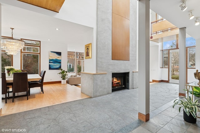 living room featuring an inviting chandelier, a high ceiling, baseboards, and a healthy amount of sunlight