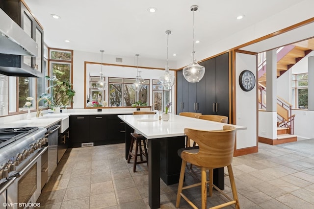 kitchen with exhaust hood, dark cabinets, visible vents, a breakfast bar, and light countertops