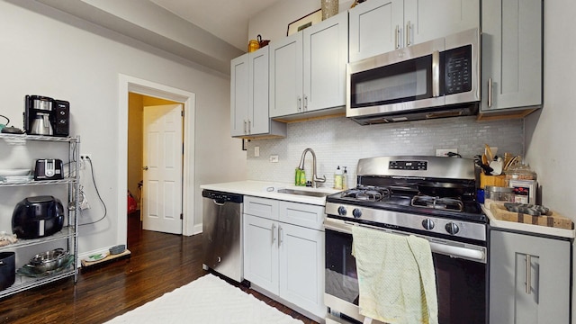 kitchen with a sink, light countertops, stainless steel appliances, dark wood-type flooring, and decorative backsplash