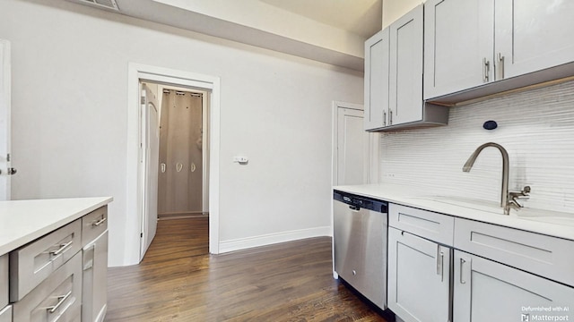 kitchen featuring dishwasher, a sink, light countertops, dark wood-style floors, and decorative backsplash