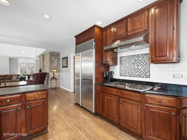 kitchen with light wood-style flooring, stainless steel appliances, open floor plan, decorative backsplash, and under cabinet range hood