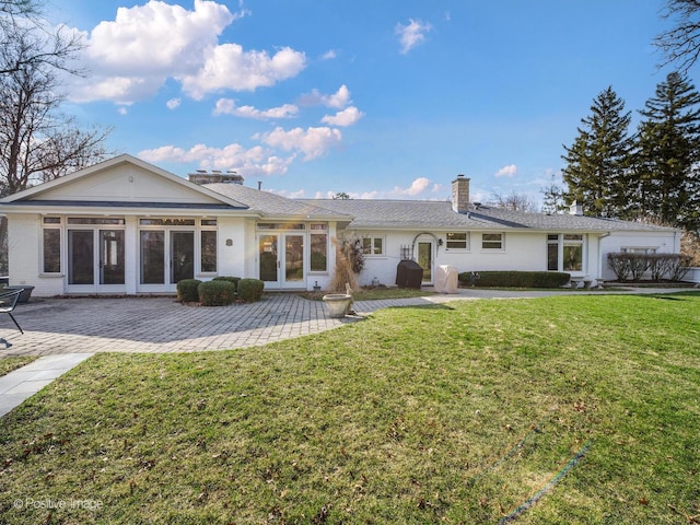 rear view of property featuring french doors, a chimney, a lawn, and a patio area