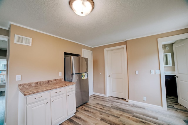 212 E Ash St, Watseka, IL 60970 - kitchen with freestanding refrigerator, a textured ceiling, light wood-type flooring, white cabinets, and crown molding