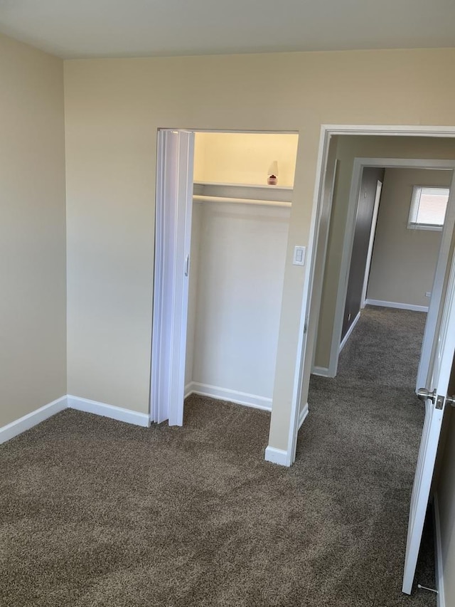 unfurnished bedroom featuring a closet, baseboards, and dark carpet