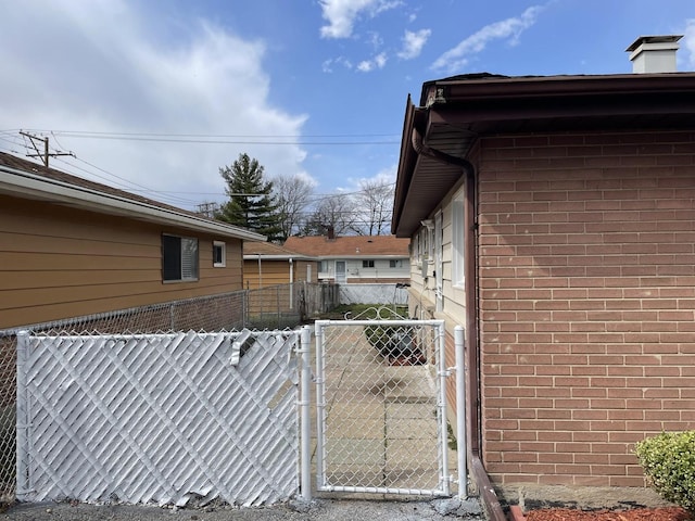 view of home's exterior featuring a chimney, brick siding, fence, and a gate