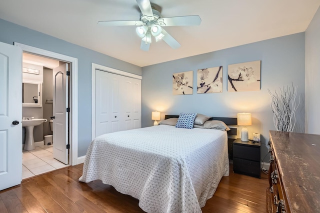 bedroom featuring a closet, ensuite bath, a ceiling fan, wood finished floors, and baseboards