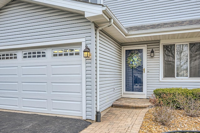 view of exterior entry with an attached garage and roof with shingles