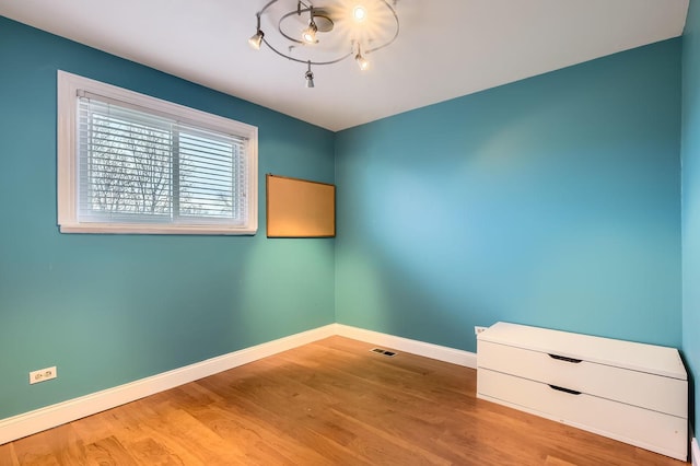unfurnished room with visible vents, baseboards, a chandelier, and wood finished floors