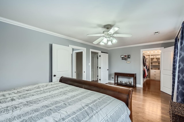 bedroom featuring a closet, ornamental molding, a spacious closet, a ceiling fan, and wood finished floors