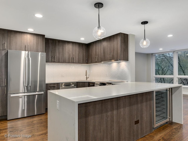 kitchen with tasteful backsplash, beverage cooler, stainless steel appliances, dark brown cabinets, and a sink