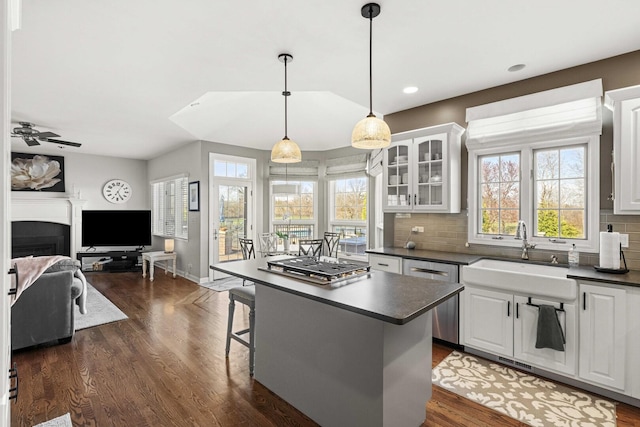 kitchen featuring glass insert cabinets, dishwasher, a sink, dark countertops, and white cabinetry