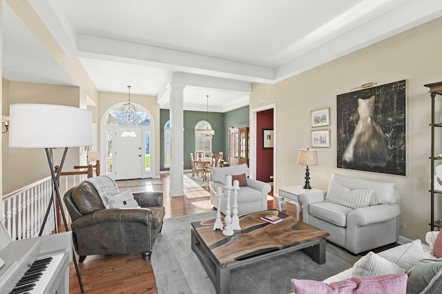 living area featuring ornate columns, wood finished floors, a notable chandelier, and baseboards