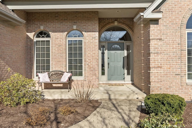 view of exterior entry featuring brick siding and covered porch