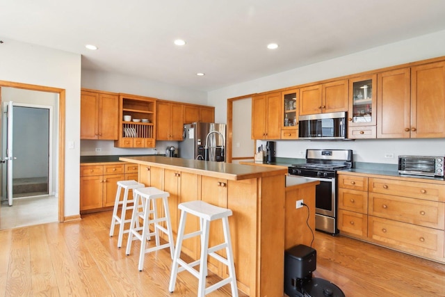 kitchen featuring open shelves, a toaster, a center island with sink, light wood-type flooring, and stainless steel appliances