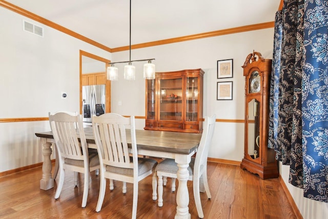 dining area featuring baseboards, visible vents, ornamental molding, and light wood finished floors