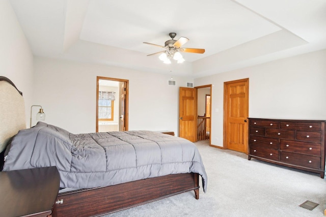 bedroom with ceiling fan, light colored carpet, visible vents, a raised ceiling, and ensuite bathroom