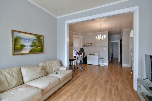 living room featuring ornamental molding, baseboards, light wood finished floors, and a chandelier