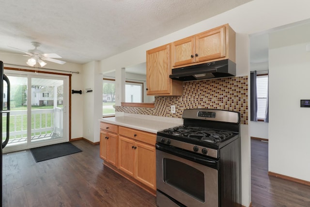 kitchen with gas stove, light countertops, baseboards, decorative backsplash, and under cabinet range hood