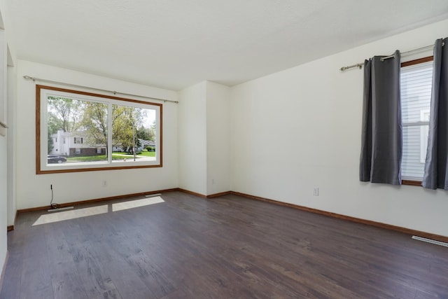 unfurnished room featuring baseboards, dark wood-style floors, and visible vents