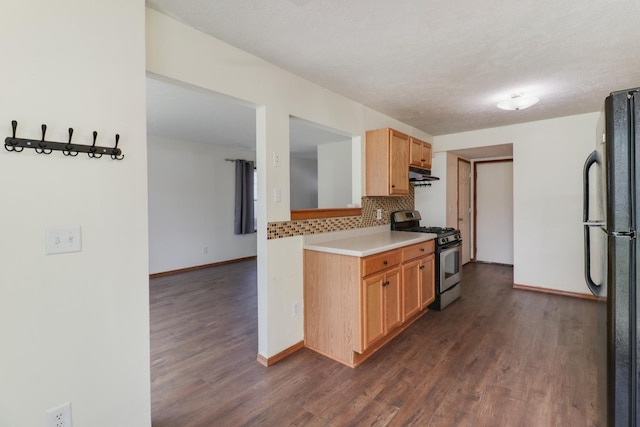 kitchen with tasteful backsplash, stainless steel gas stove, freestanding refrigerator, under cabinet range hood, and dark wood-type flooring