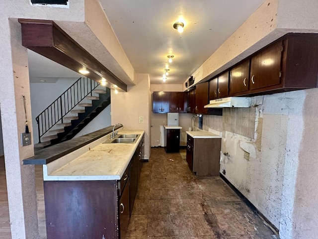 kitchen with dark brown cabinetry, range hood, light countertops, and a sink