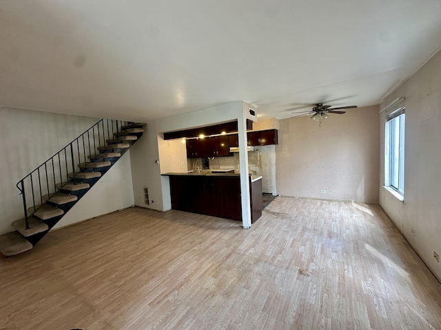 unfurnished living room featuring stairs, light wood finished floors, and ceiling fan