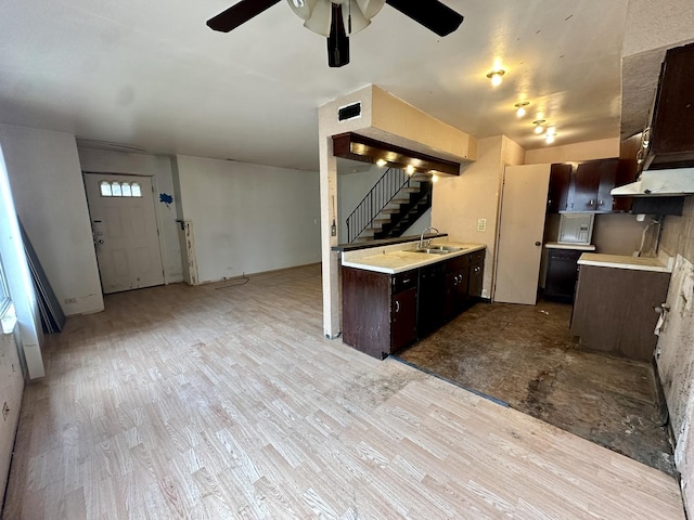 kitchen with dark brown cabinetry, a ceiling fan, wood finished floors, a sink, and light countertops