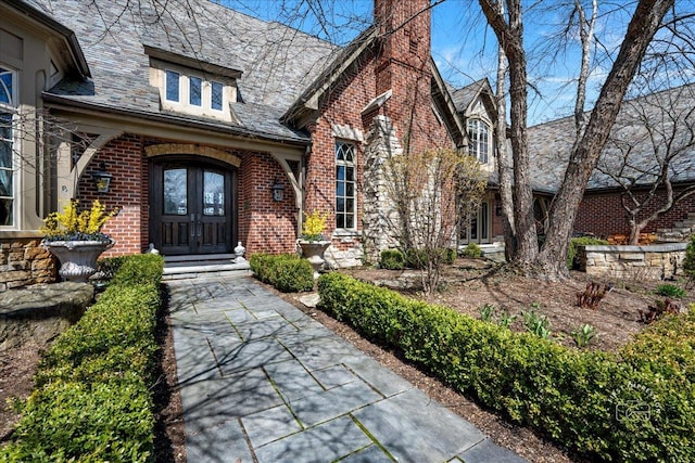 36W442 Hunters Gate Rd, Saint Charles, IL 60175 - view of exterior entry with french doors, a chimney, brick siding, and a high end roof