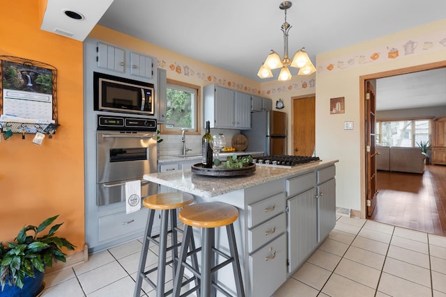 kitchen with a notable chandelier, a center island, a warming drawer, light tile patterned flooring, and stainless steel appliances