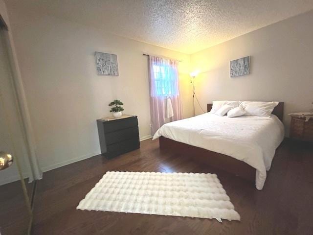 bedroom with a textured ceiling, wood finished floors, and baseboards