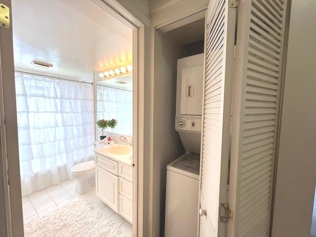 bathroom featuring toilet, tile patterned floors, stacked washer / dryer, and vanity