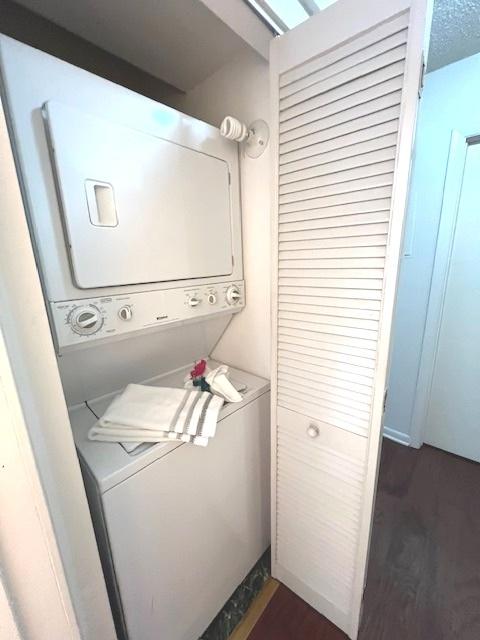 clothes washing area with dark wood finished floors, laundry area, and stacked washer and clothes dryer